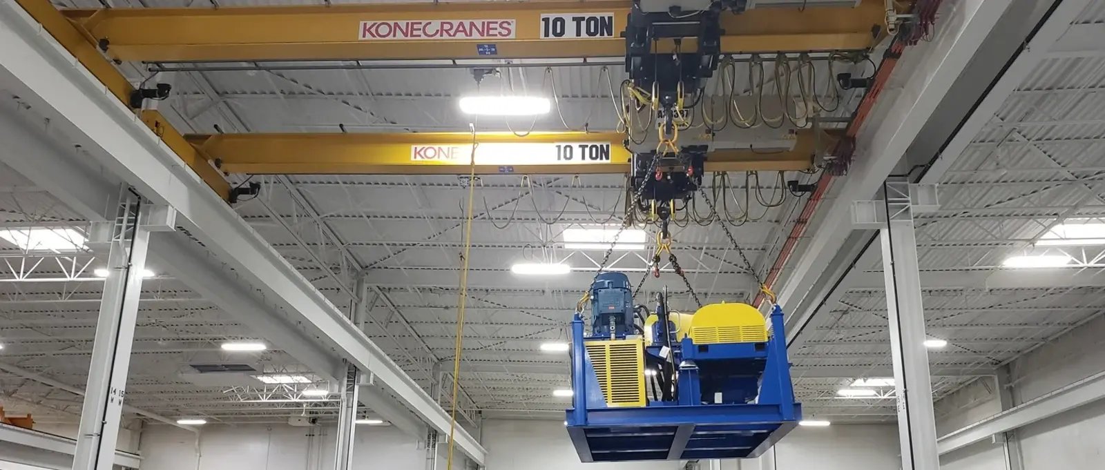 An overhead crane lifts a decanter centrifuge inside a repair facility.